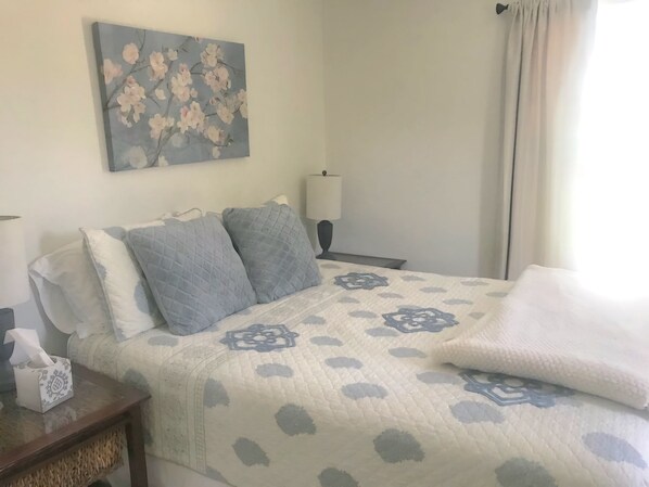 Una cama bien hecha con una colcha estampada, una mesita de noche con una caja de pañuelos y una lámpara de pared.