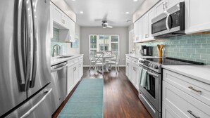 A modern kitchen with stainless steel appliances, white cabinetry, a dining area with a table and chairs, and a view through a window. - Newly updated 2B/2B condo, walk to the beach! (Holmes Beach)
