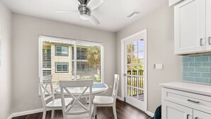 A kitchen with white cabinets, a white dining table with chairs, a ceiling fan, and a view of the outdoors through the windows. - Newly updated 2B/2B condo, walk to the beach! (Holmes Beach)
