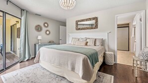 A bedroom with a large bed, a ceiling light, a mirror, and a door leading to a bathroom. - Newly updated 2B/2B condo, walk to the beach! (Holmes Beach)