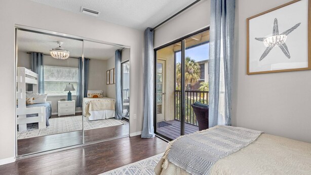 A bedroom with a large mirror, a bed with a patterned blanket, and a view of a balcony with a starfish artwork. - Newly updated 2B/2B condo, walk to the beach! (Holmes Beach)