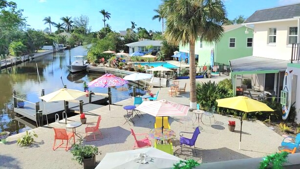 A waterfront patio with outdoor seating and umbrellas, a pool, and a palm tree.