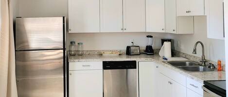 A modern kitchen with white cabinets, stainless steel appliances, and a granite countertop.