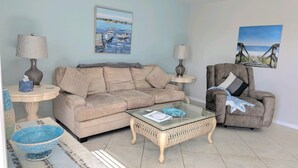 A living room with a beige sofa, a glass coffee table, a wicker armchair, and two lamps.