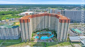 A high-rise hotel with a central courtyard featuring a swimming pool, surrounded by lush greenery and additional buildings.