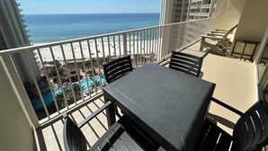 A balcony with a table and chairs, overlooking a beach and a pool.