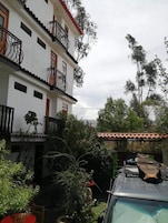 Um edifício de vários andares com varandas, um pátio com vegetação e um veículo estacionado.