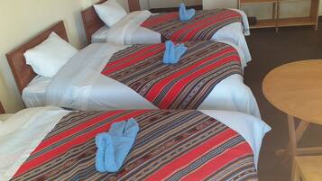 A hotel room with three beds, each with a red and white striped bedspread and blue towels. There is a wooden table in the room.