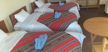 A hotel room with three beds, each with a red and white striped bedspread and blue towels. There is a wooden table in the room.