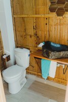 A bathroom with a wooden wall, a white toilet, a stone basin, and a towel hanging on a rack.