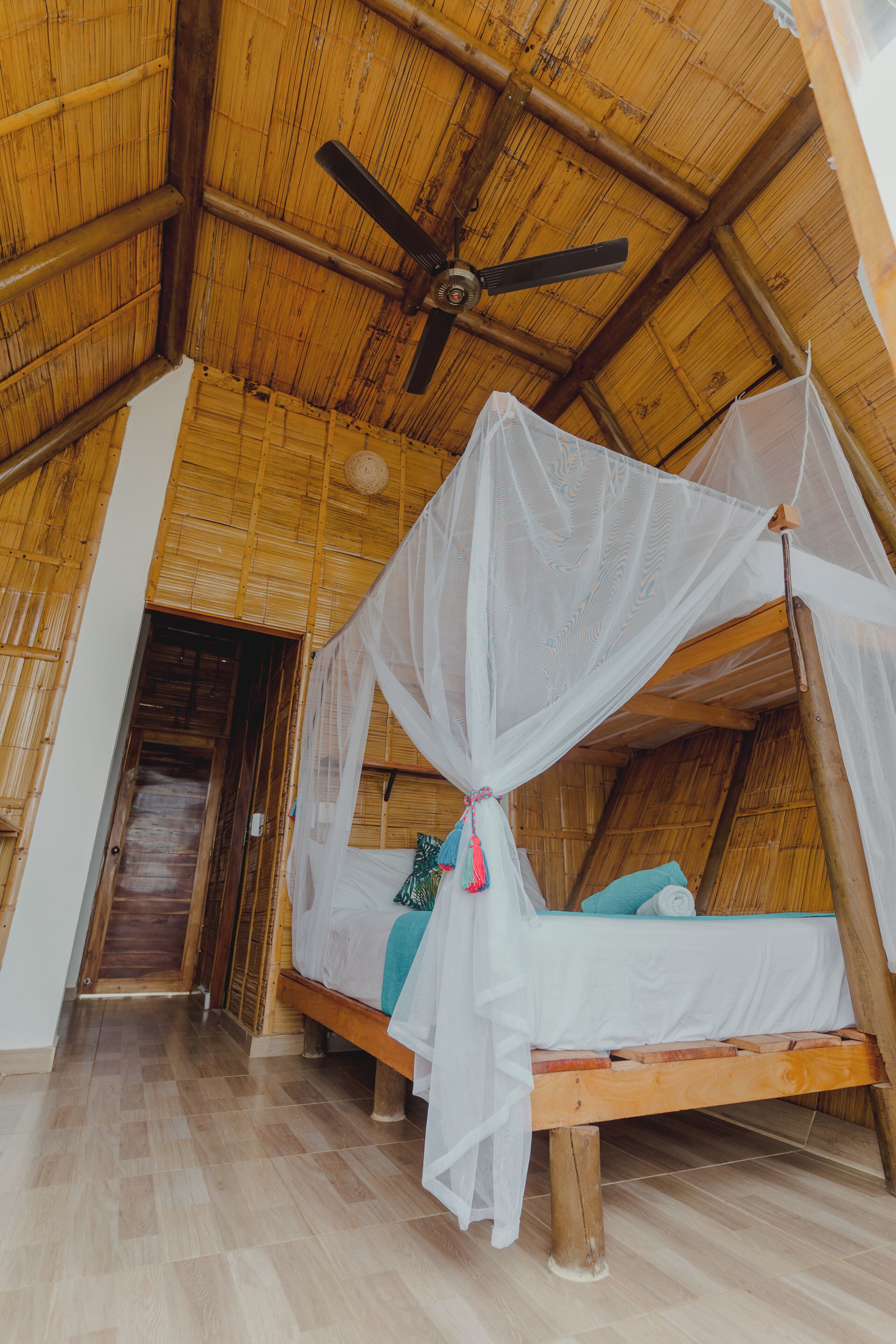 A room with a bed under a mosquito net, a ceiling fan, and a wooden floor.