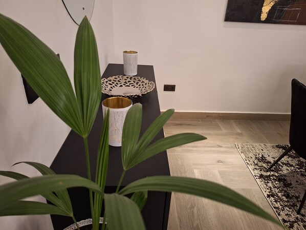 Un coin repas moderne avec une table noire, un vase blanc agrémenté de motifs dorés et une assiette décorative.