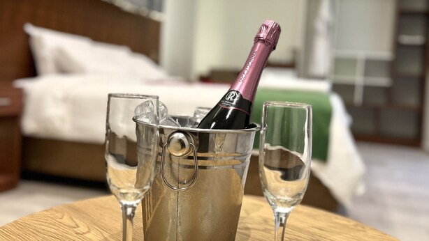 A room with a bed, a bedside table with a champagne bottle and glasses, and a green bedspread. - HOTEL EL ALAMO EJECUTIVO & SPA (Cusco)