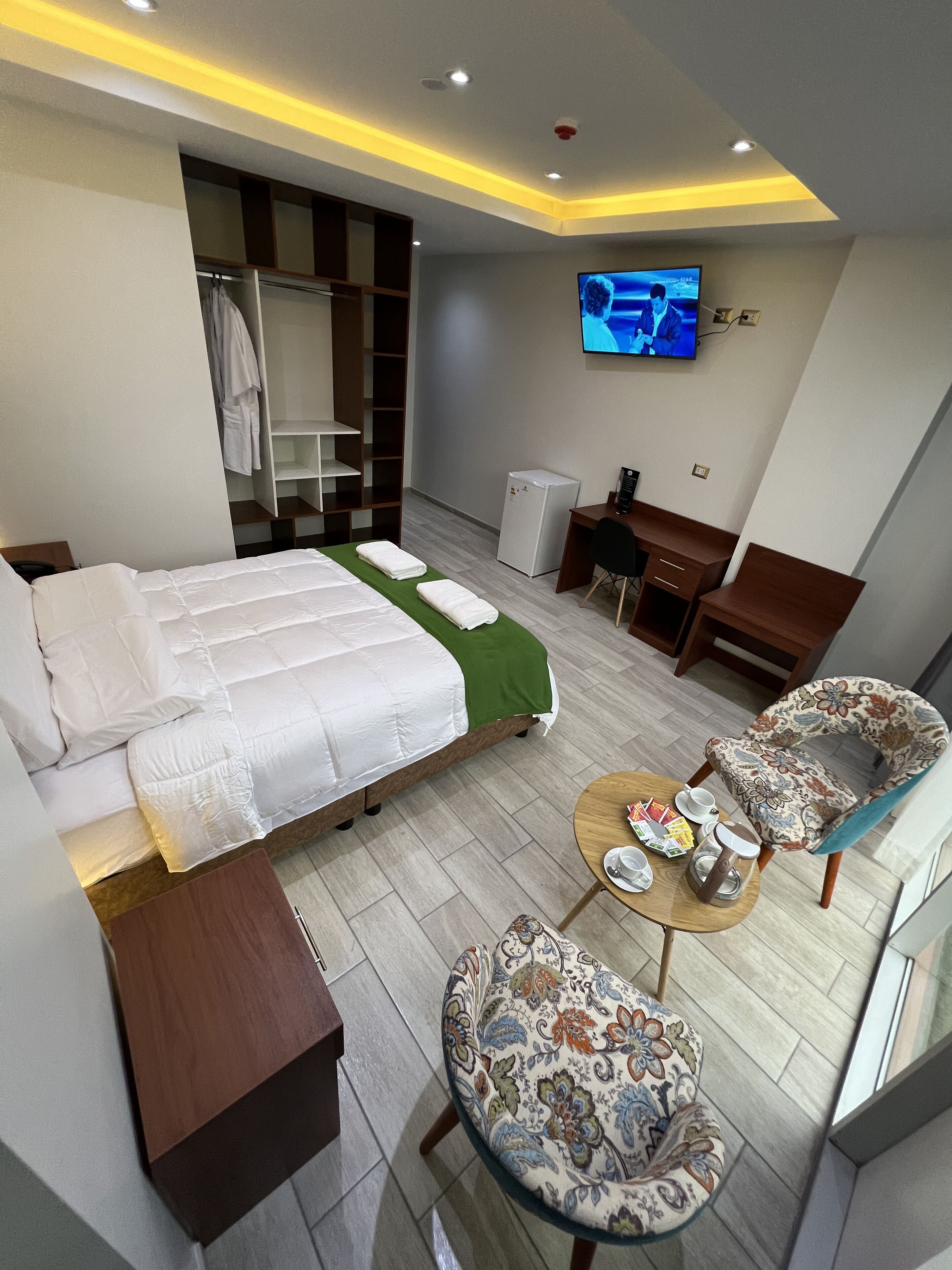 A hotel room with a bed, a desk, a chair, a TV, and a small refrigerator.