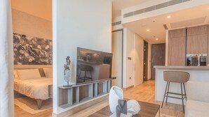 Ein modernes Wohnzimmer mit einer Couch, einem Couchtisch und einem Fernseher. Es gibt eine Küchenzeile mit Holzschränken und einem Barhocker.