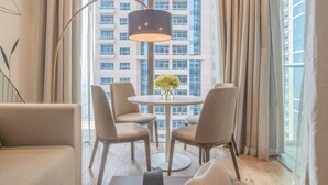 Ein modernes Hotelzimmer mit einem runden Tisch, vier Stühlen, einer Stehlampe und Blick auf einen Hochhaus durch große Fenster.