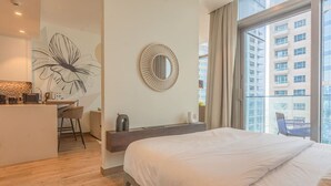 Ein modernes Hotelzimmer mit einem großen Bett, einem Schreibtisch mit Stuhl, einem großen Fenster mit Blick auf Gebäude und einem Wandspiegel.