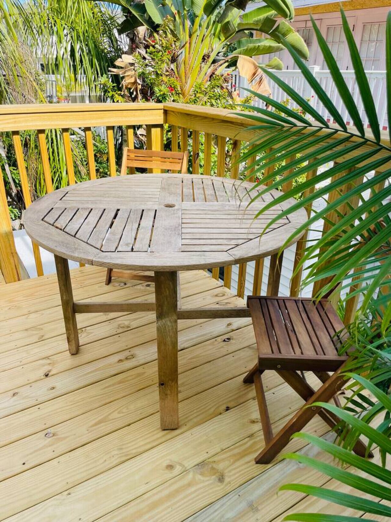 Une terrasse circulaire en bois, avec une table et des chaises, entourée d’une balustrade en bois et d’une végétation luxuriante.