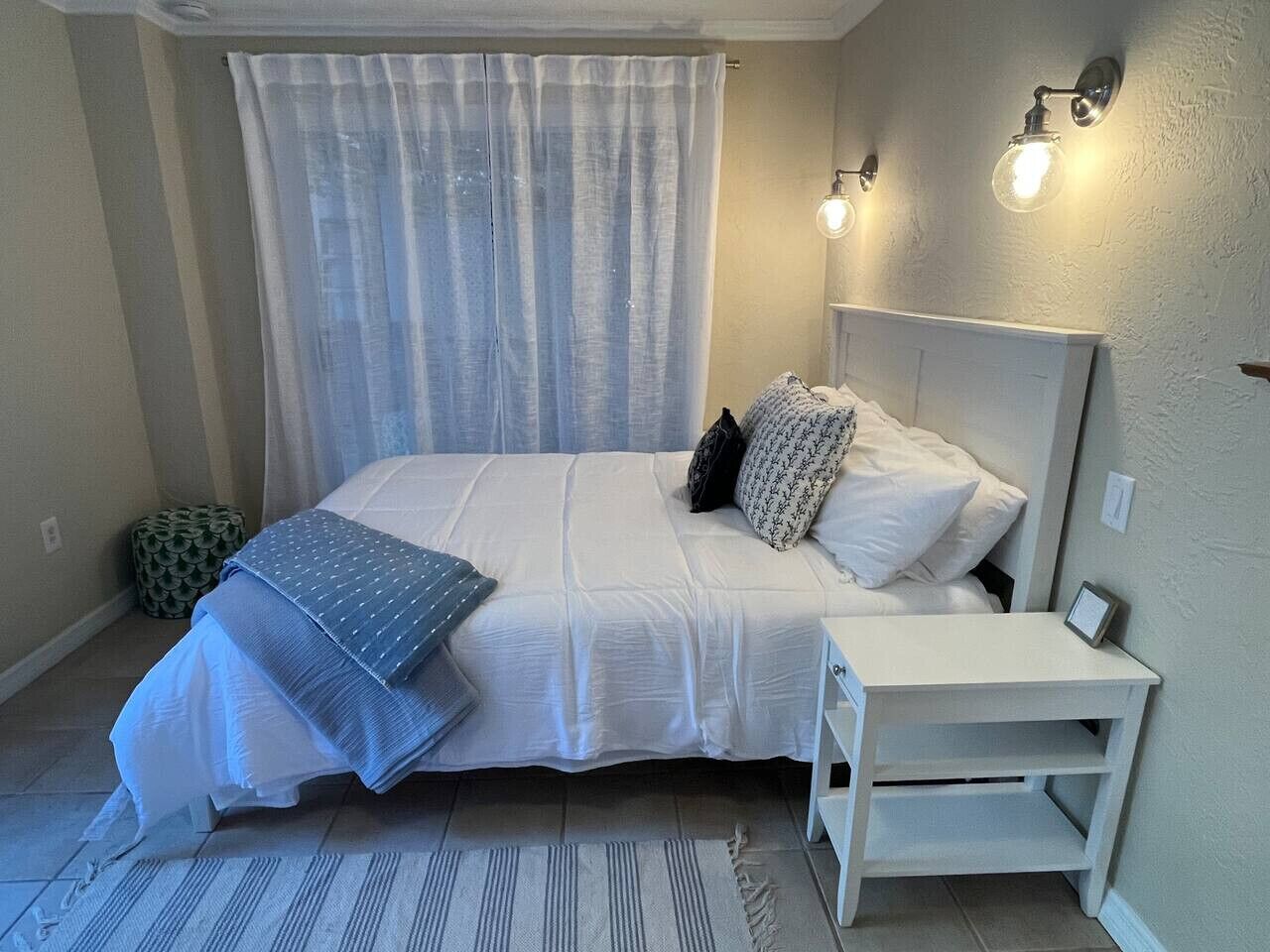 A bedroom with a bed, bedside table, and a window with curtains.
