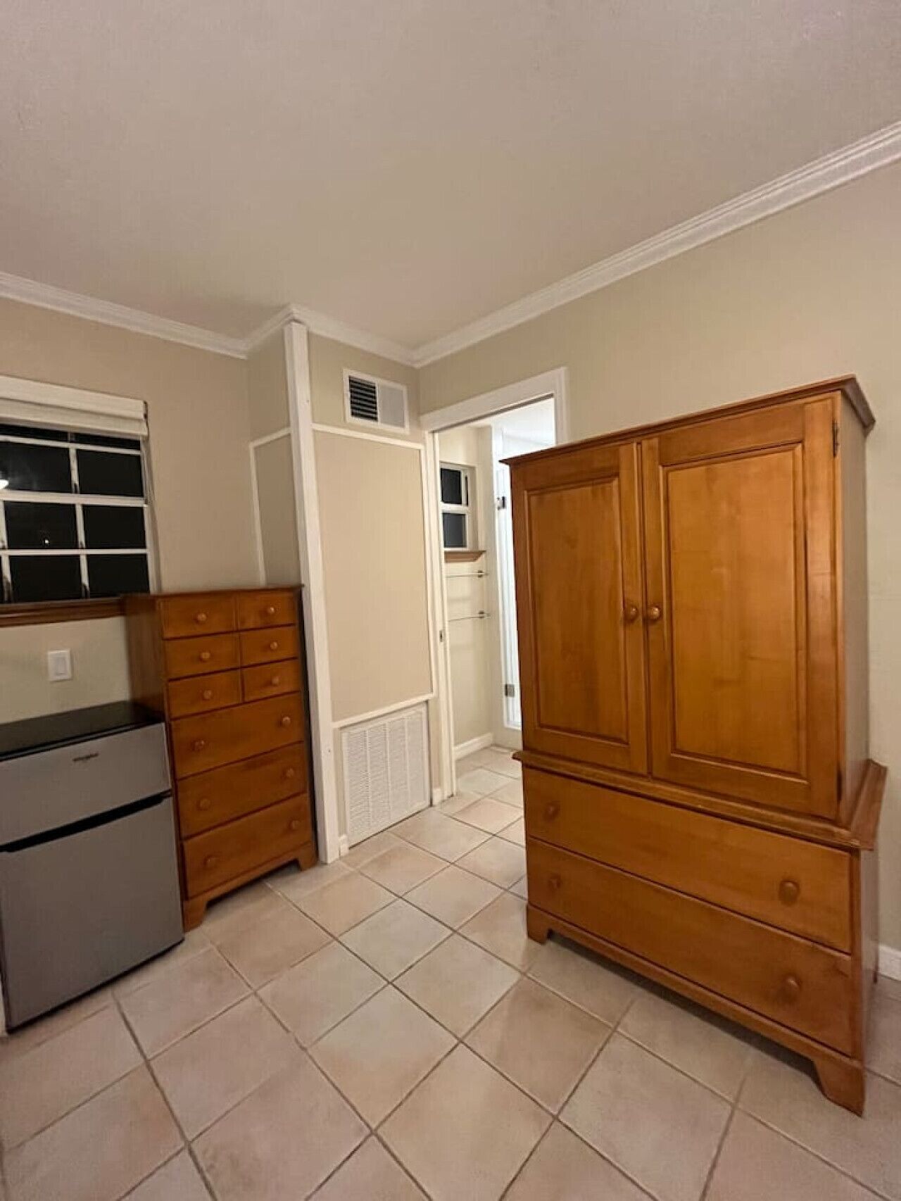 A kitchen with a refrigerator, wooden cabinets, and a tiled floor.