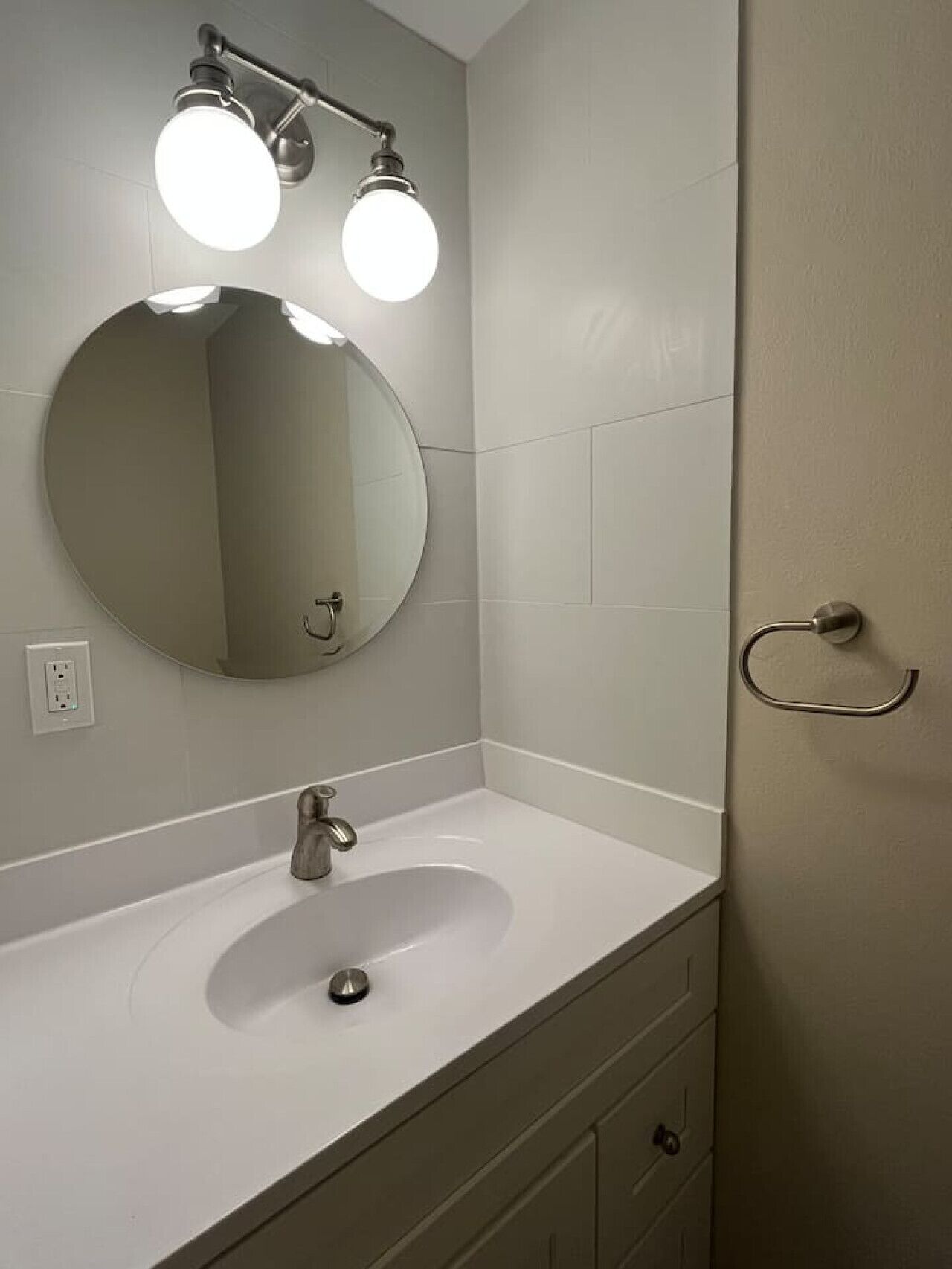 Un baño con un espejo redondo, dos luces en el techo, un lavabo y una puerta.