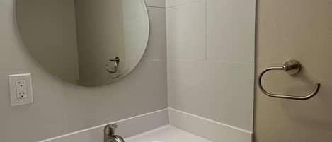 Un baño con un espejo redondo, dos luces en el techo, un lavabo y una puerta.