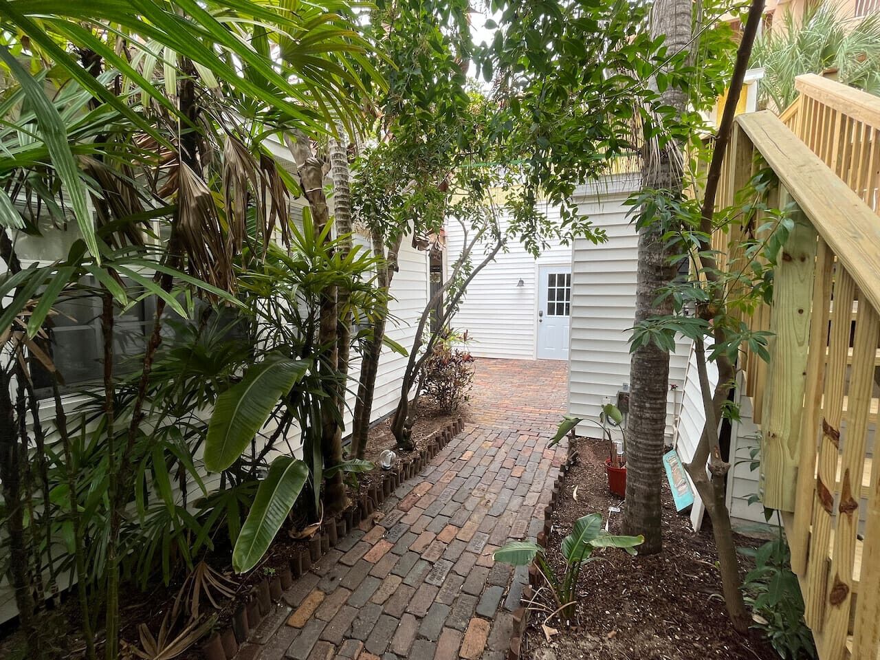 A narrow brick pathway leading to a white building with a wooden fence on one side.
