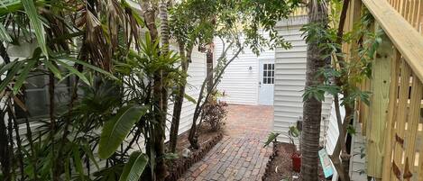 A narrow brick pathway leading to a white building with a wooden fence on one side.
