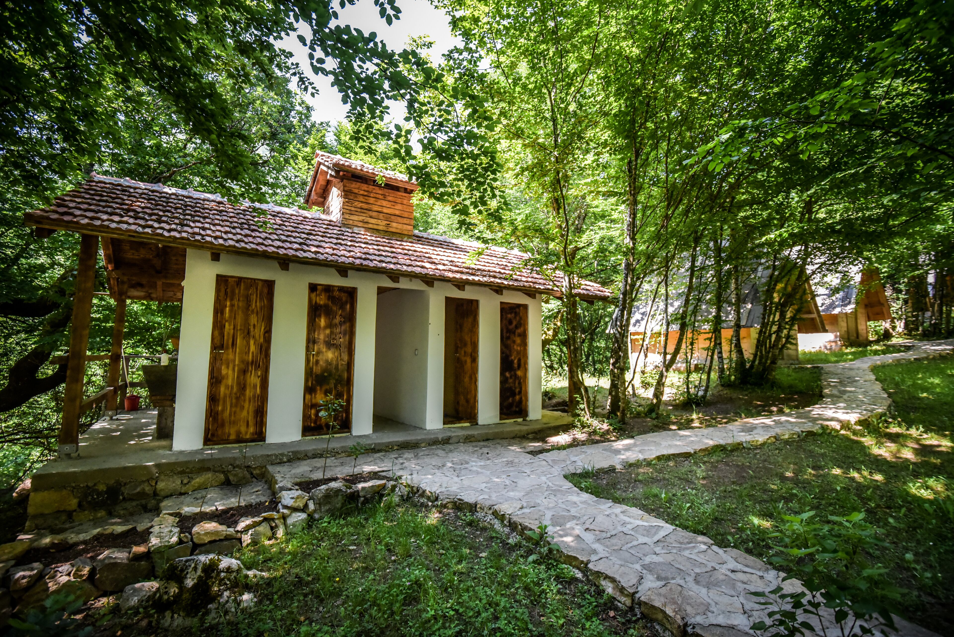 A rustic building with a tiled roof, wooden doors, and a stone pathway leading to it.