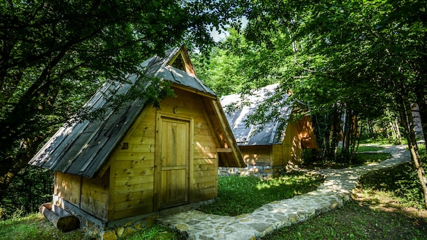 A rustic wooden cabin with a stone pathway leading to it, surrounded by lush greenery. - Camp Divlja Rijeka (Foca)