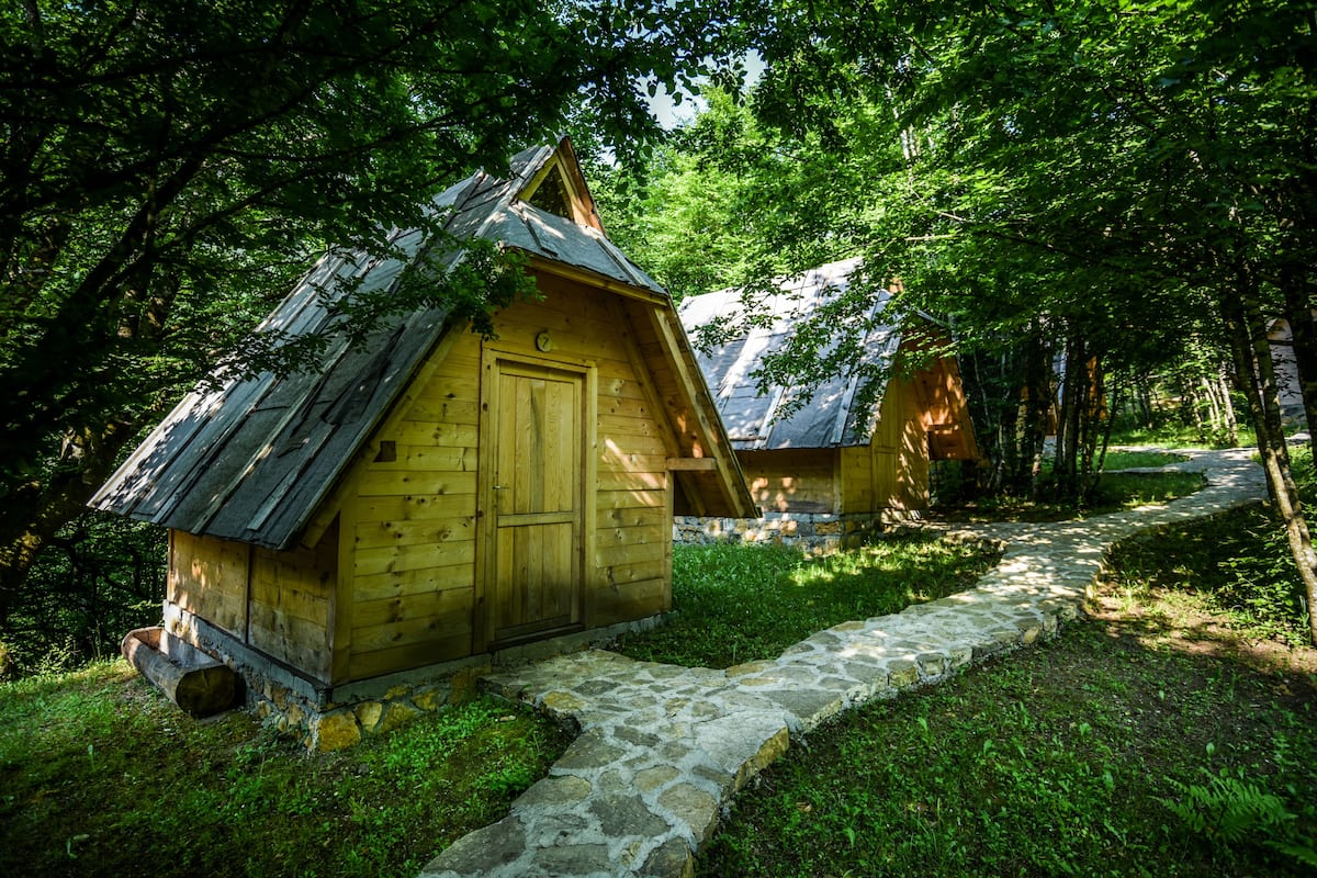 A rustic wooden cabin with a stone pathway leading to it, surrounded by lush greenery.