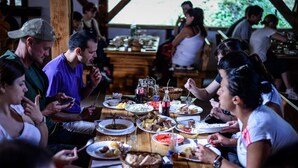 A group of people dining at a wooden table with various dishes and drinks. - Camp Divlja Rijeka (Foca)