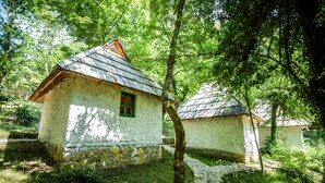 A rustic wooden cabin with a stone foundation, surrounded by lush greenery and a stone pathway. - Camp Divlja Rijeka (Foca)