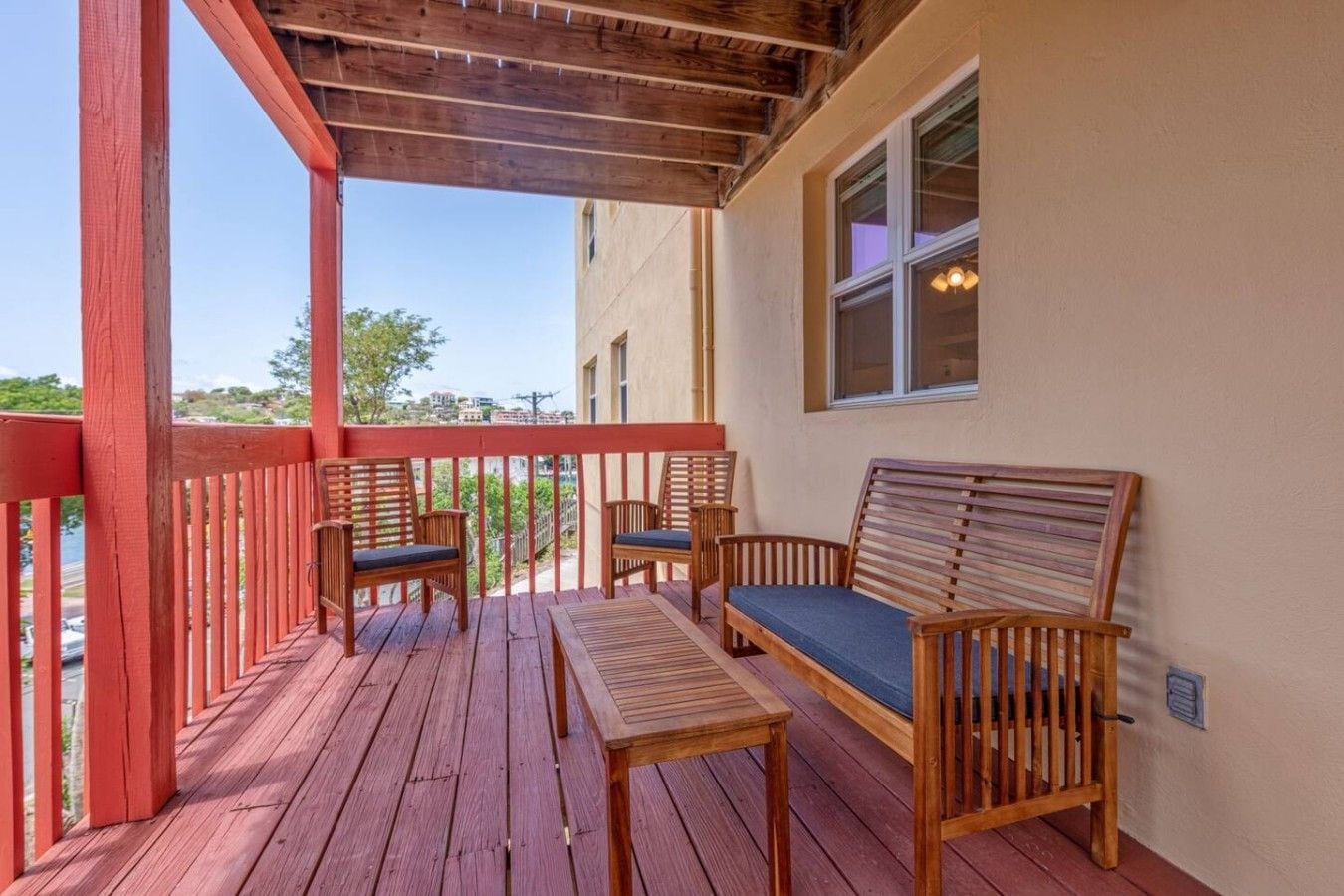 Une terrasse en bois avec une rambarde rouge, un banc et deux chaises.