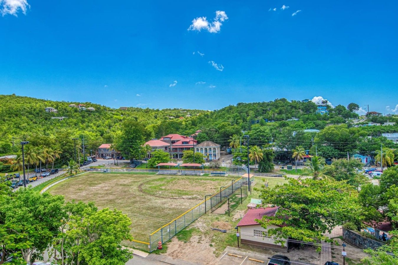 A residential area with a large house, a fenced sports field, and surrounding greenery.