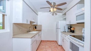A compact kitchen with white cabinets, a sink, a stove, and a ceiling fan.
