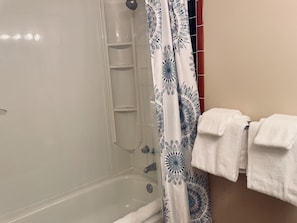 A shower area with a glass door, a white bathtub, and a patterned shower curtain.