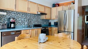 A modern kitchen with wooden cabinets, a tiled backsplash, stainless steel appliances, and a wooden dining table. - Spacious Town Home, Sleeps 8, Walk to Gondola! (Whistler)