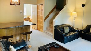A living room with a wooden bar, leather sofas, a staircase, and a dining area in the background. - Spacious Town Home, Sleeps 8, Walk to Gondola! (Whistler)