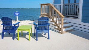 Een terras aan het strand met twee blauwe Adirondack-stoelen, een groene tafel en een bordje met de tekst 'STAY OFF ROCKS'.