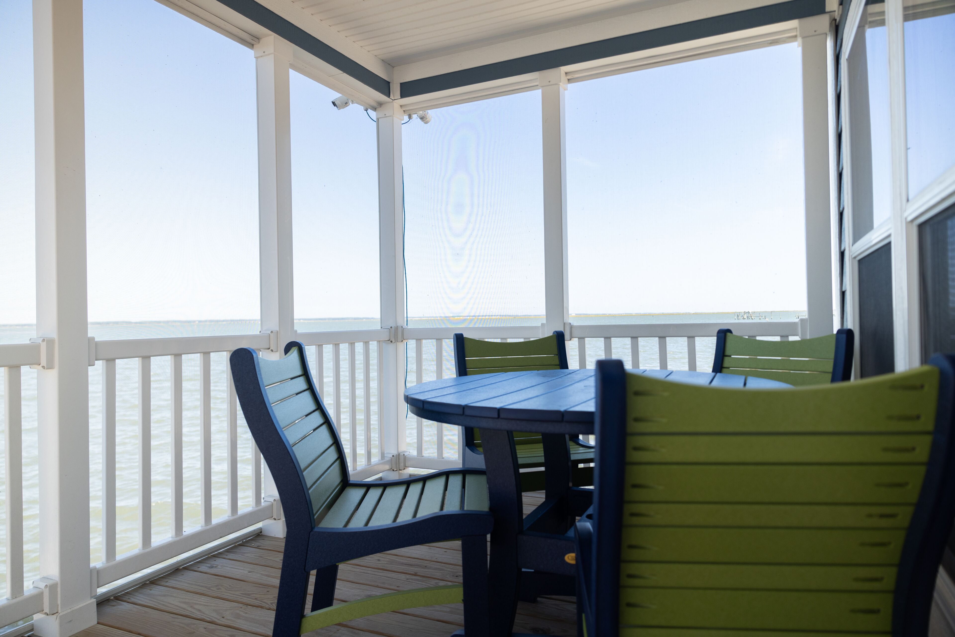 A covered outdoor area with a wooden deck, white railings, and a table with chairs.