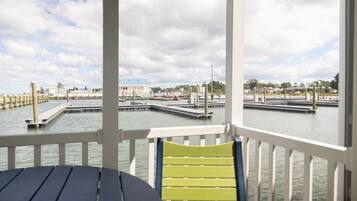 Une vue depuis une terrasse couverte, avec une table et des chaises, donnant sur une marina avec des quais et des bateaux.