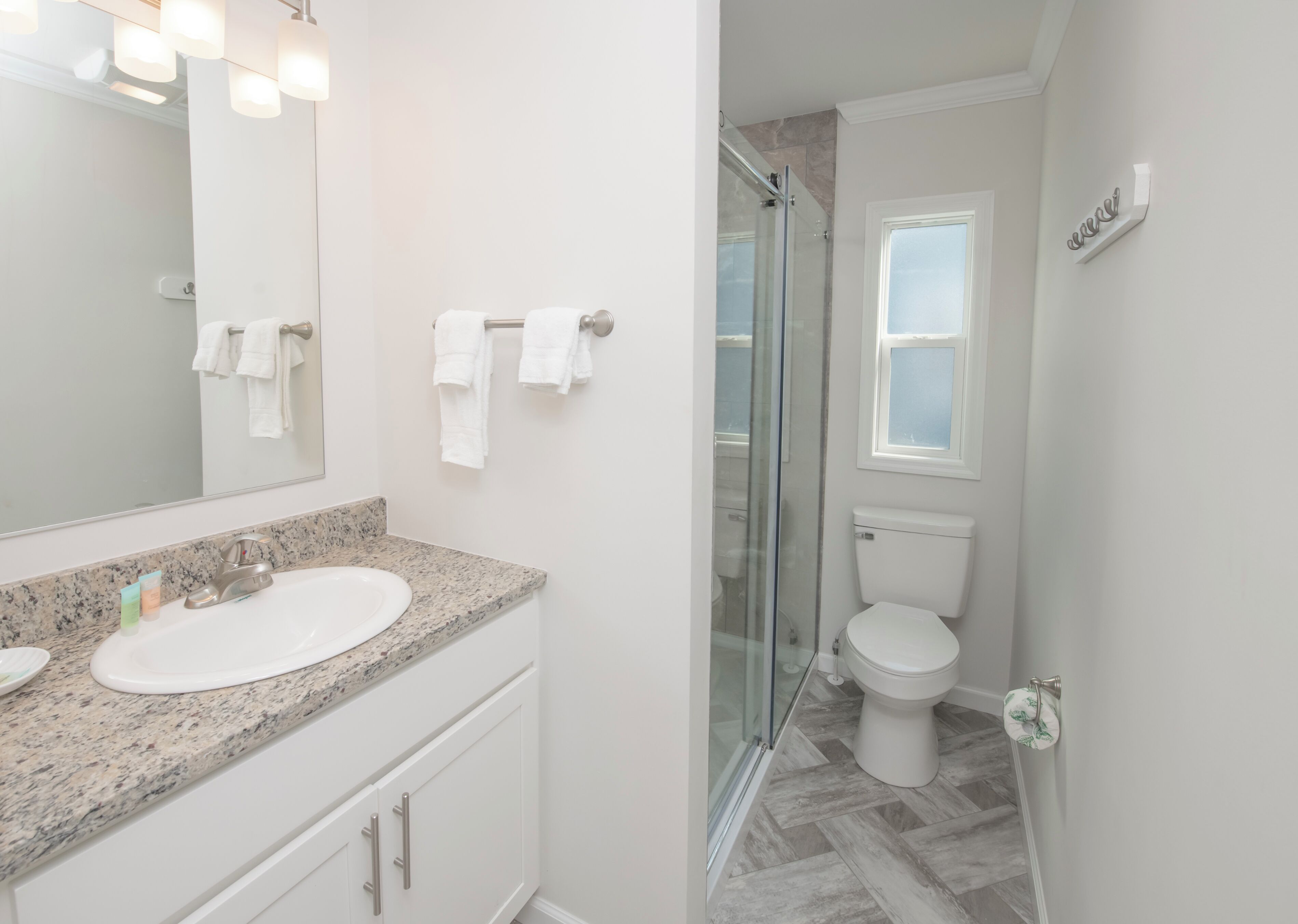 Un baño con encimera de granito, un lavabo, un inodoro y una cabina de ducha de vidrio.