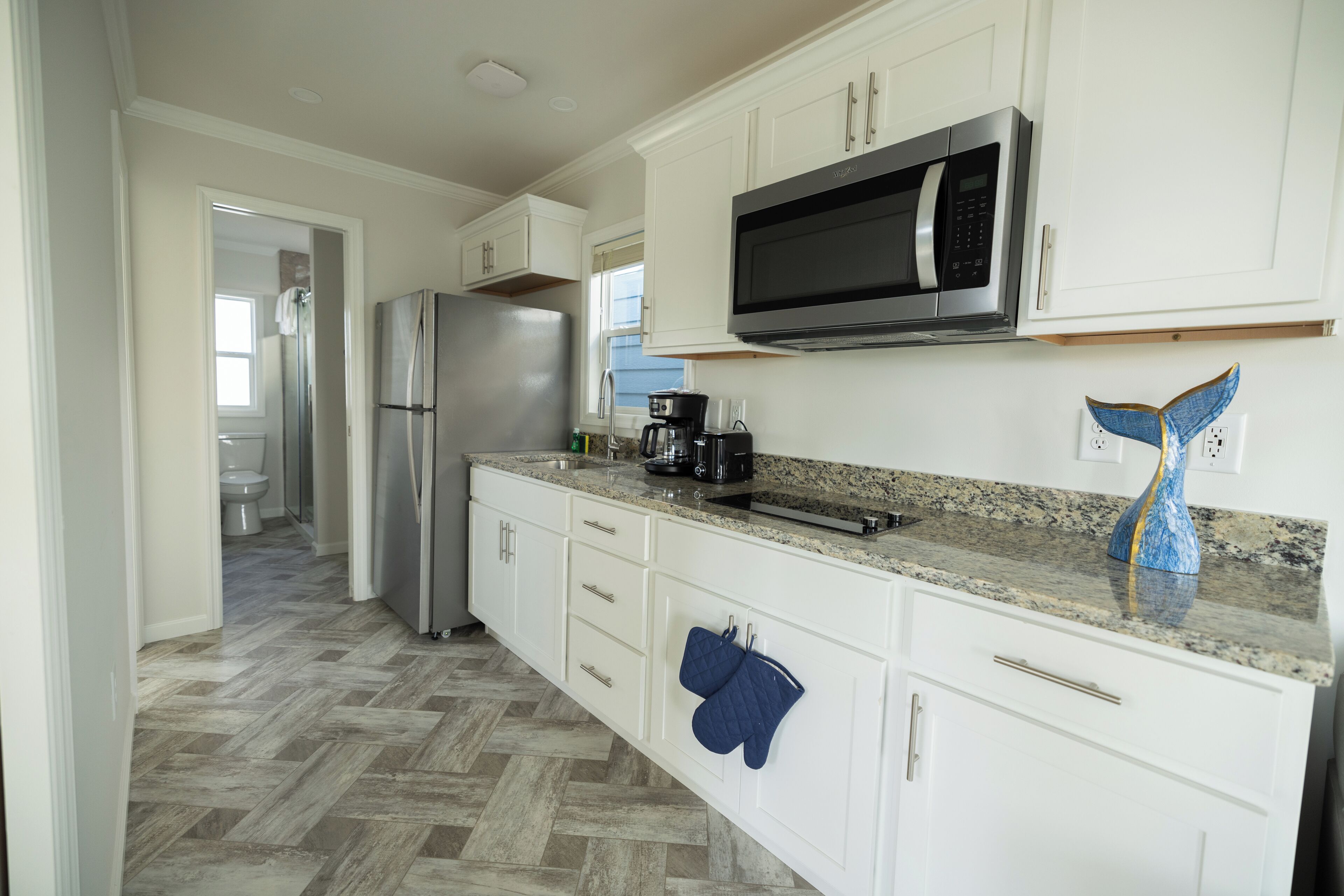 A kitchen with white cabinets, a stainless steel refrigerator, a microwave, and a granite countertop.