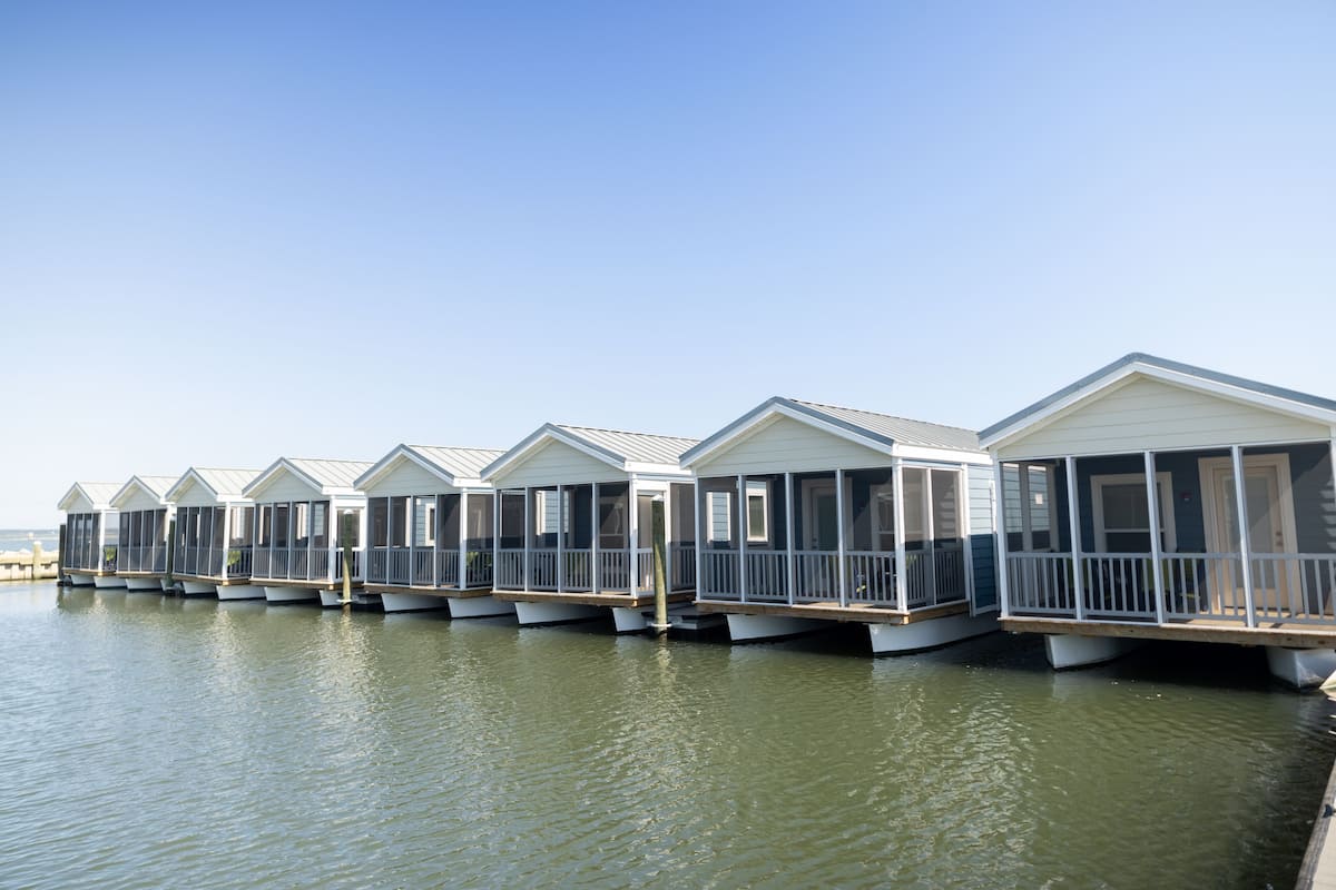 Une rangée de maisons flottantes dotées de balcons, reliées par des passerelles, sur une étendue d’eau calme.