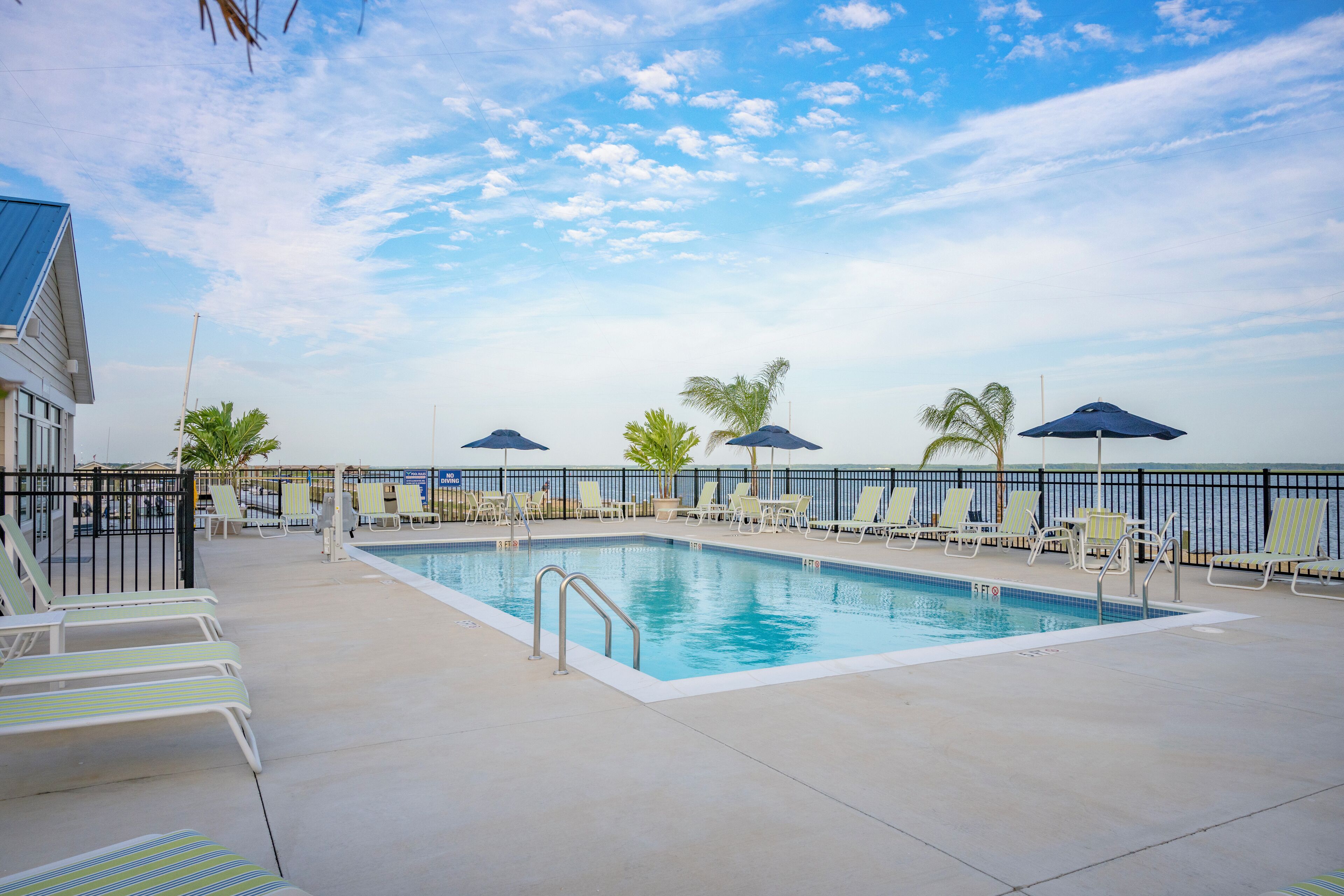 A pool area with lounge chairs and umbrellas, a clear sky, and a view of the ocean.