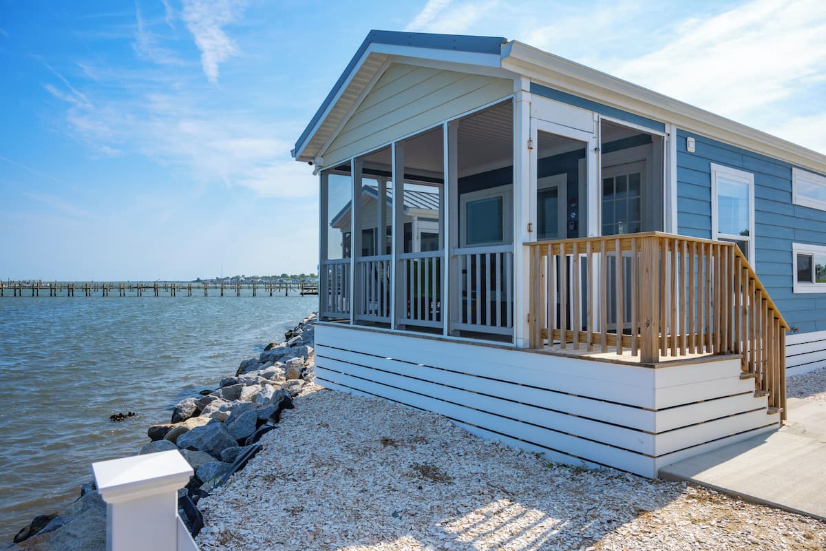 Une maison située sur la côte, dotée d’une terrasse en bois, de grandes fenêtres et offrant une vue sur l’eau.