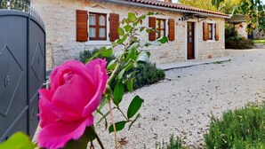 A stone house with a gravel driveway and a pink rose in the foreground.