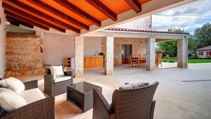 A covered outdoor patio with wicker furniture, stone pillars, and a stone wall.