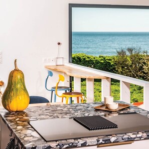 Una cocina con encimera de piedra, una calabaza grande y vistas al mar a través de una ventana.